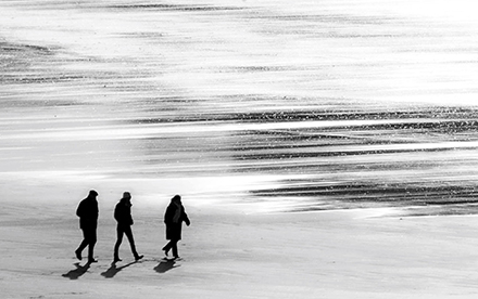 Photo en noir et blanc de Marilg : 3 silhouettes de marcheurs sur la plage