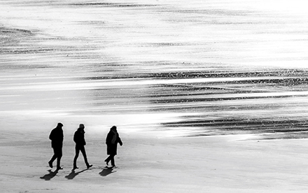 Photo en noir et blanc de Marilg : 3 silhouettes de marcheurs sur la plage